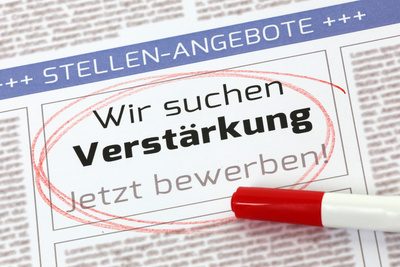 Eine Zeitungsanzeige im Bereich 'Stellenangebote' ist rot eingekreist. Der Text der Anzeige lautet: 'Wir suchen Verstärkung - Jetzt bewerben'. Vor der Anzeige liegt ein roter Stift, der den Kreis markiert hat.